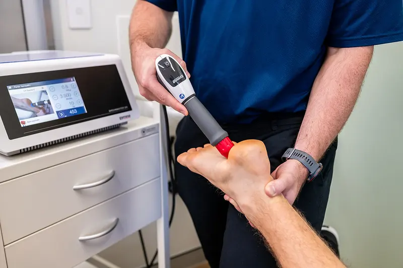 A clinician using a handheld treatment device on a patient’s foot